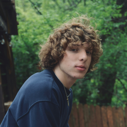 Teenage boy leaning over a fence with trees in the background