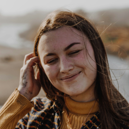 Teenage girl brushing hair away from her face while her eyes are closed, smiling